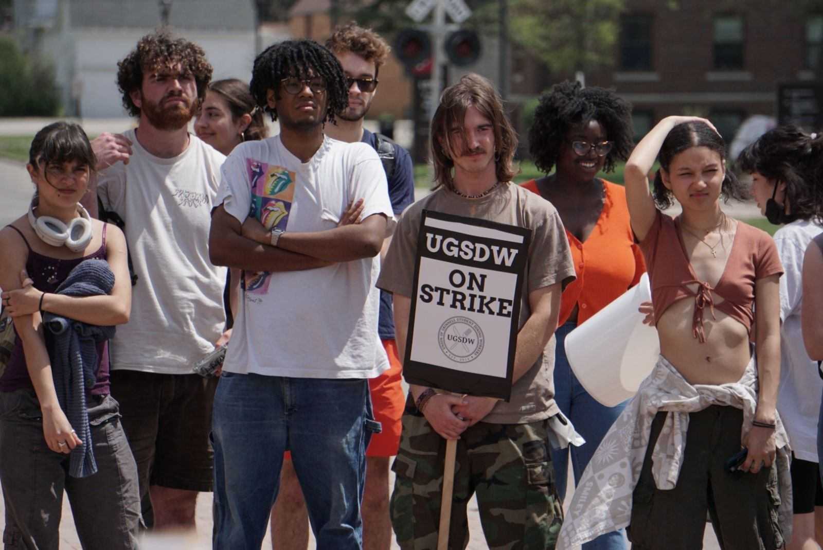 A photograph of several student workers standing. One holds a sign reading "UGSDW on strike"