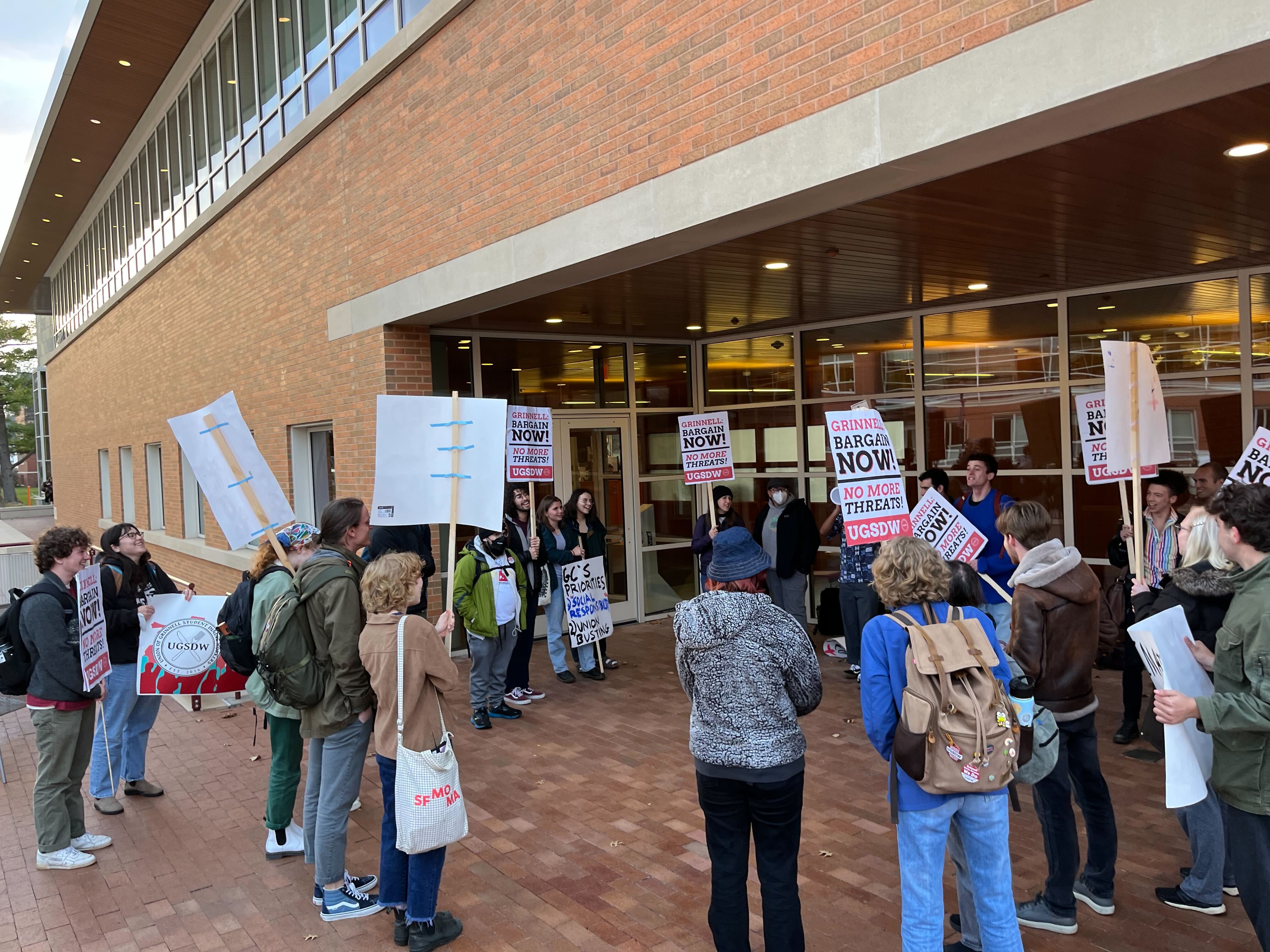 A group of student workers stands in a circle outside the JRC, holding pro-union signs