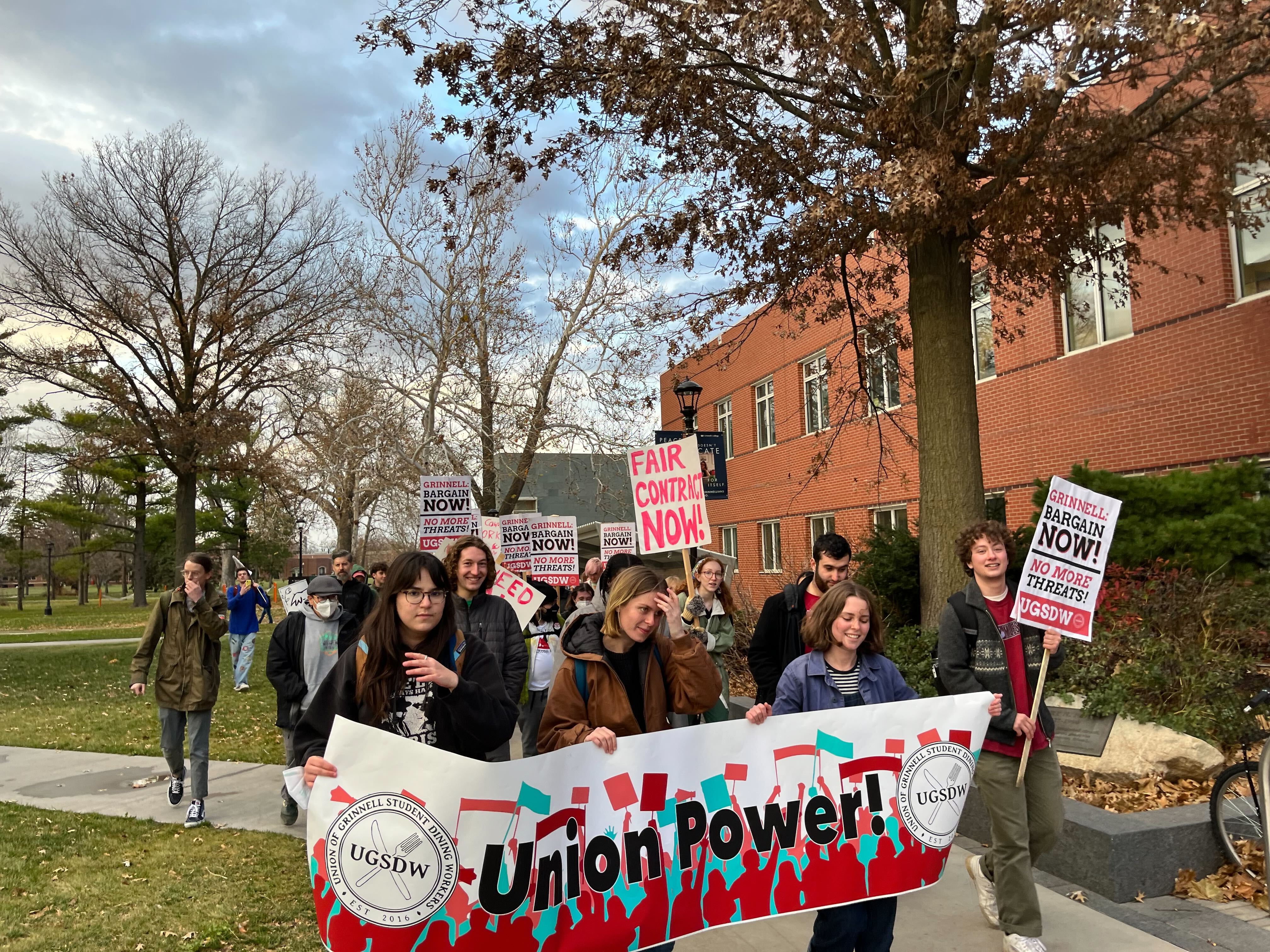 A large group of student workers marches across campus carrying pro-union signs and banners