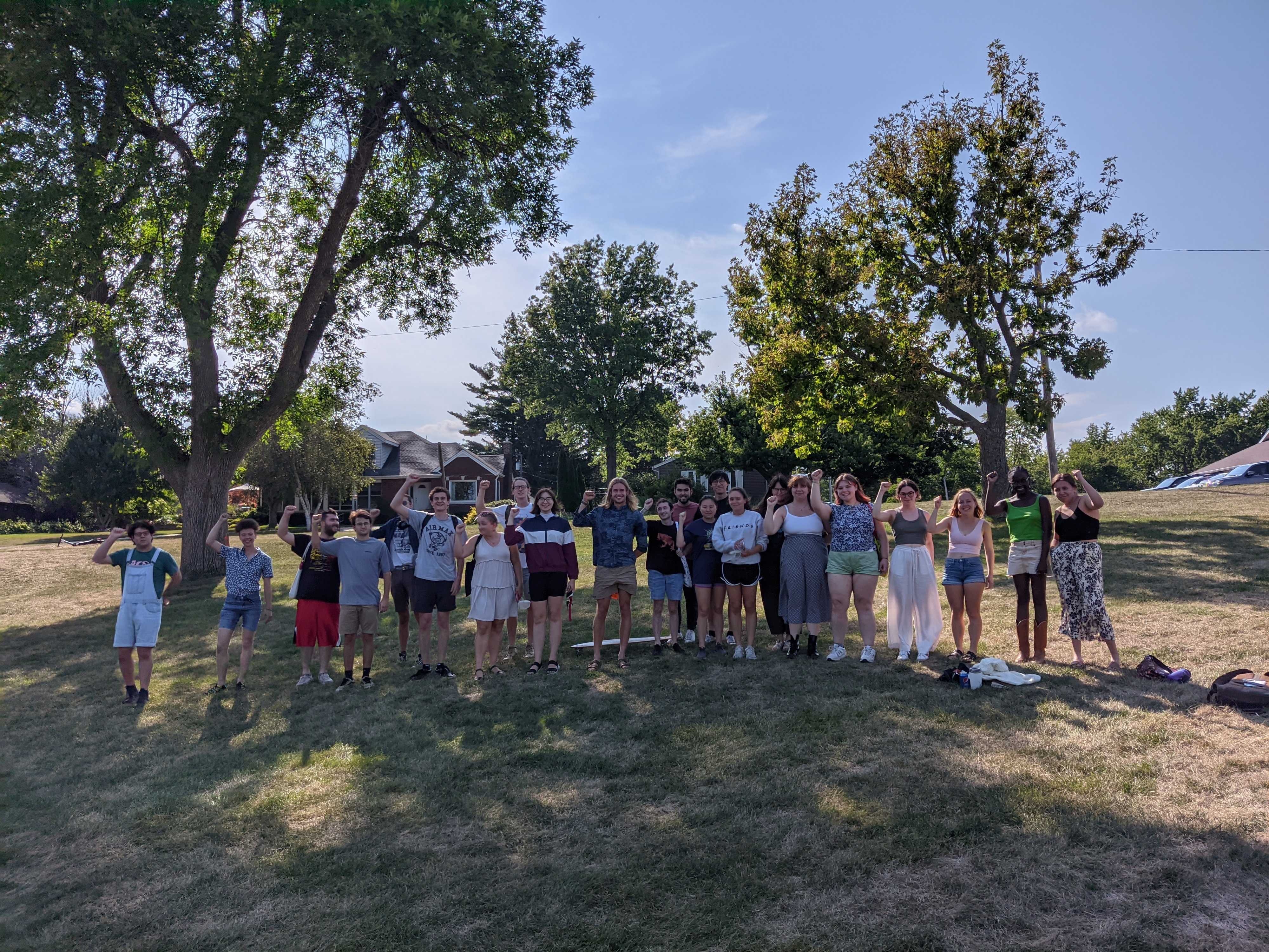 A photograph of several student-workers standing on a lawn, raising their fists