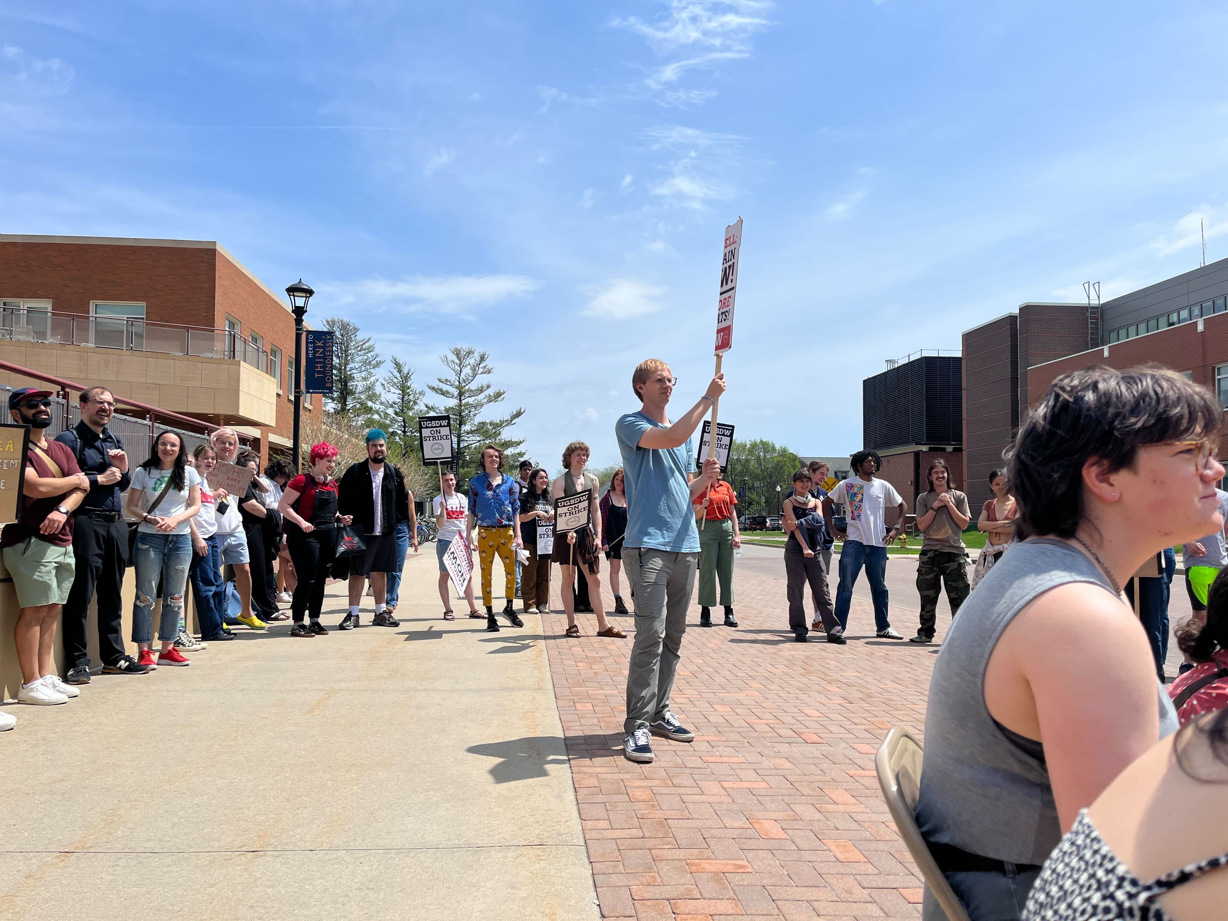 A photograph of several Grinnell students standing in a circle, two holding signs reading "UGSDW on strike"